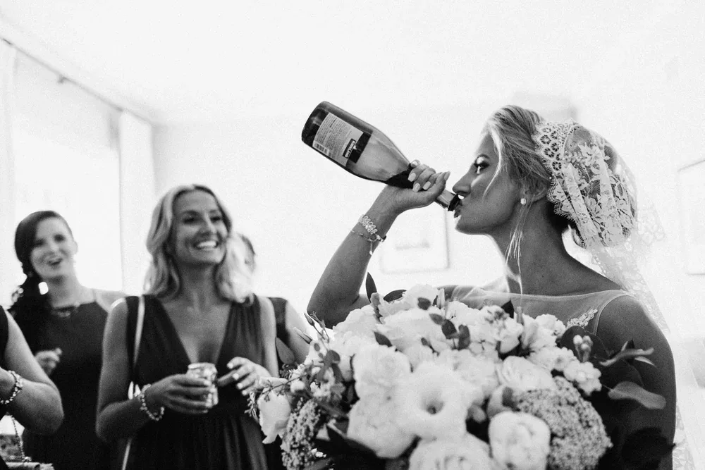 Black and white photo of the bride drinking champagne from the bottle beside her bridesmaids at the Beauport Hotel