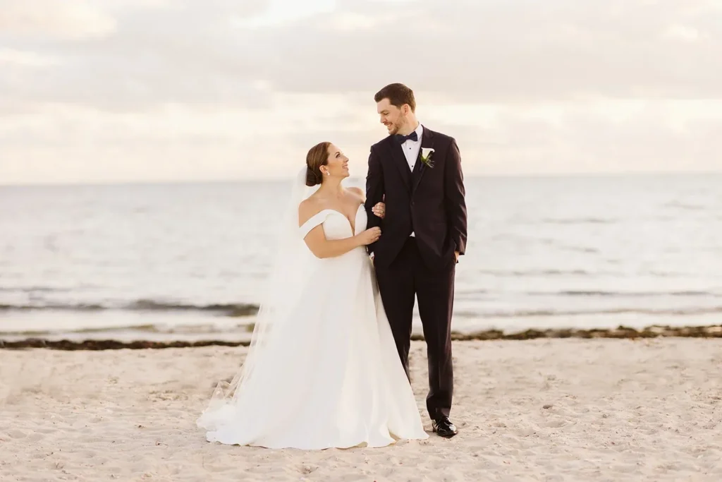 Bride and groom stand together on the private beach at Wychmere Beach Club with Nantucket Sound behind them
