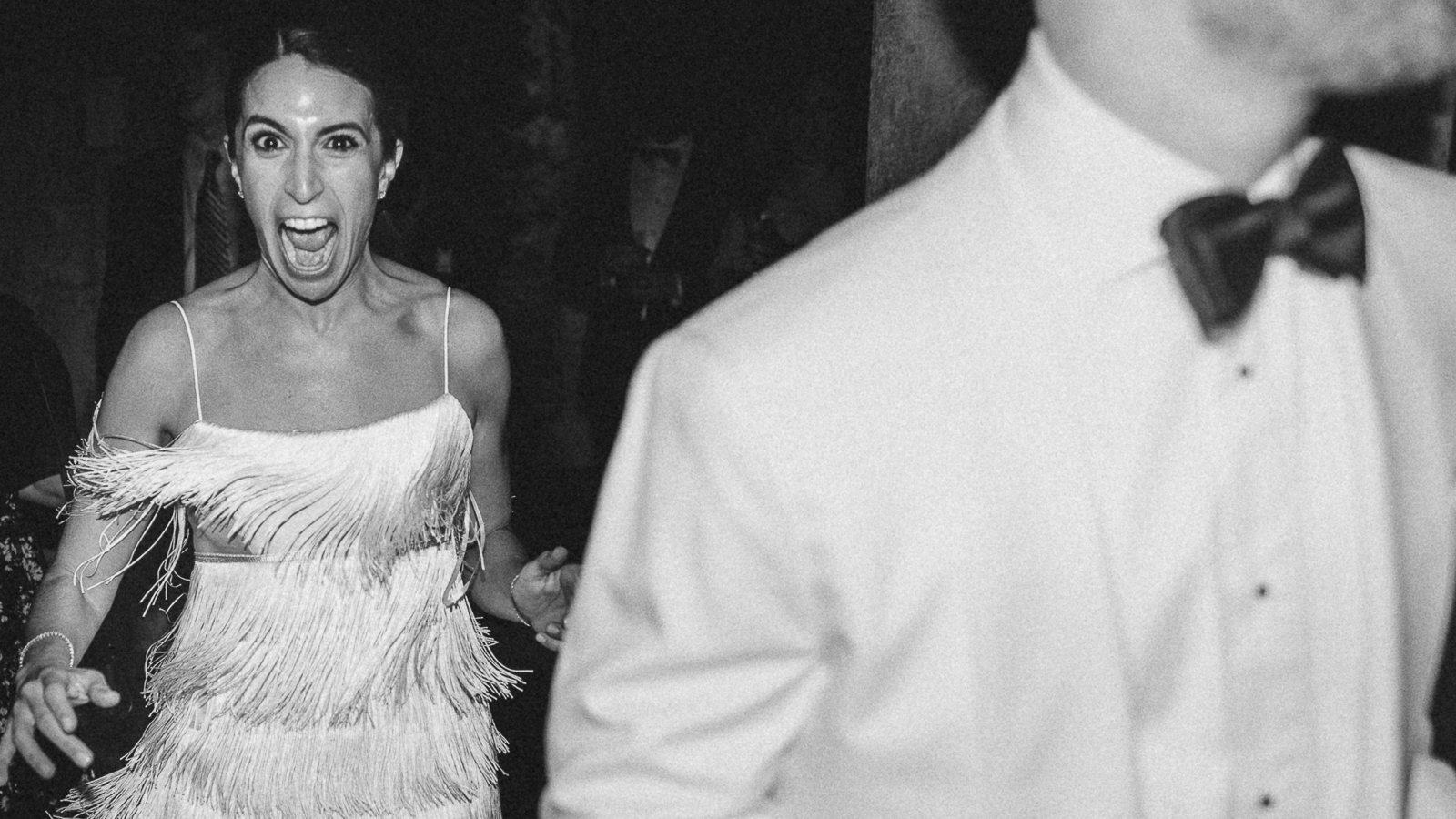 Mastering Direct Flash for Bold, Editorial Wedding Photos (2025 Trend) 1 Laughing woman in fringe dress reacts behind blurred tuxedoed groom