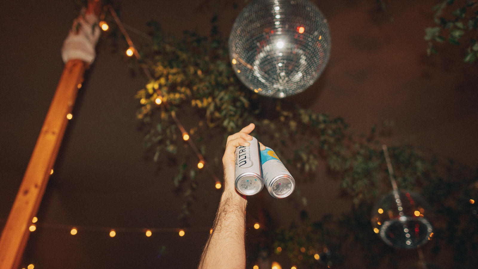 Essential Wedding Photography Equipment Check List 1 Hand raises two beer cans toward disco ball under string lights