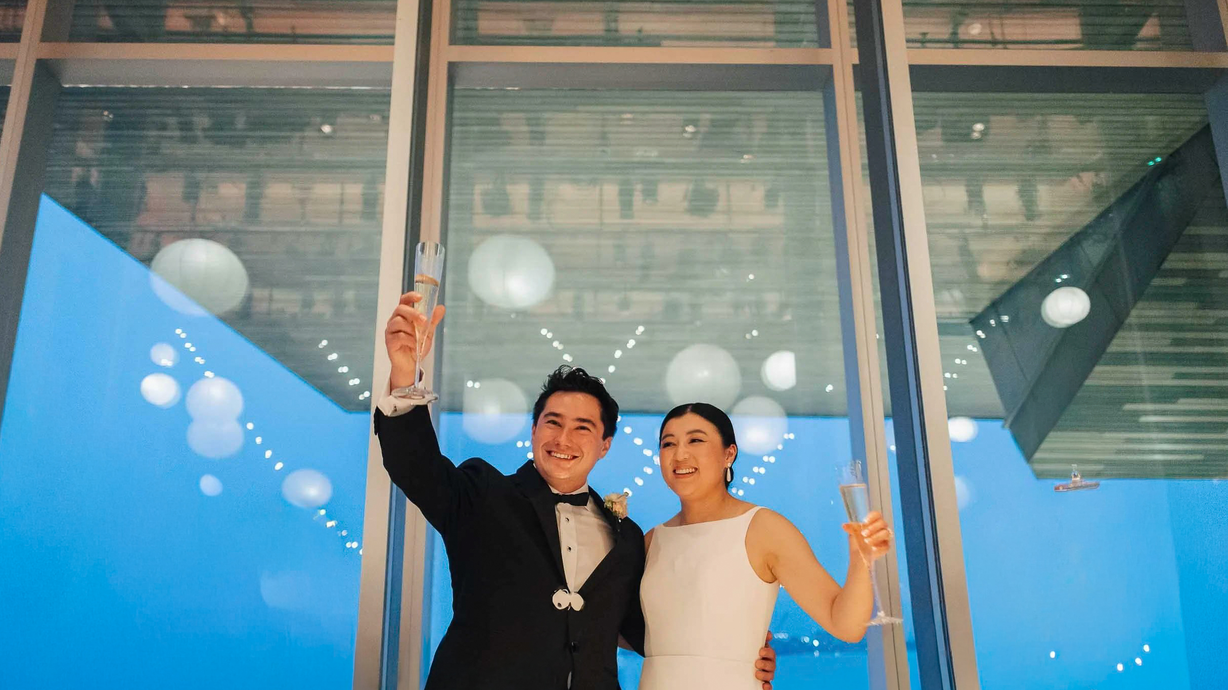 The Cost of a Boston Wedding Photographer in 2025 1 Couple toasting champagne beneath tall windows and hanging lanterns