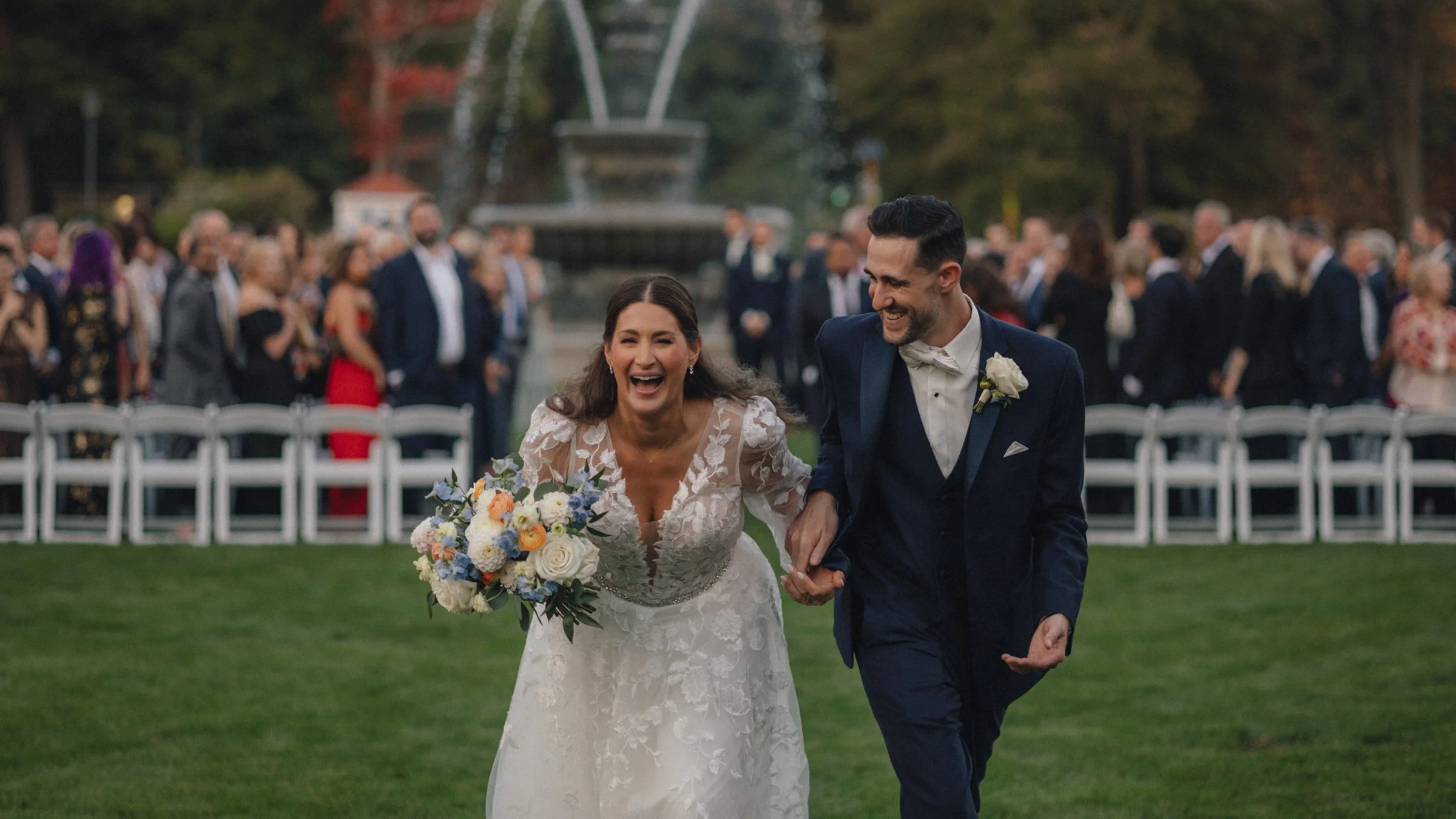 Boston Elopement Planning Guide For 2025 1 Laughing couple recess across lawn, fountain and guests behind