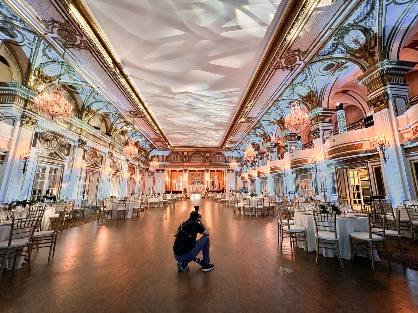 Eric kneeling alone in the middle of a chandeliered ballroom to photograph the room before guests arrive