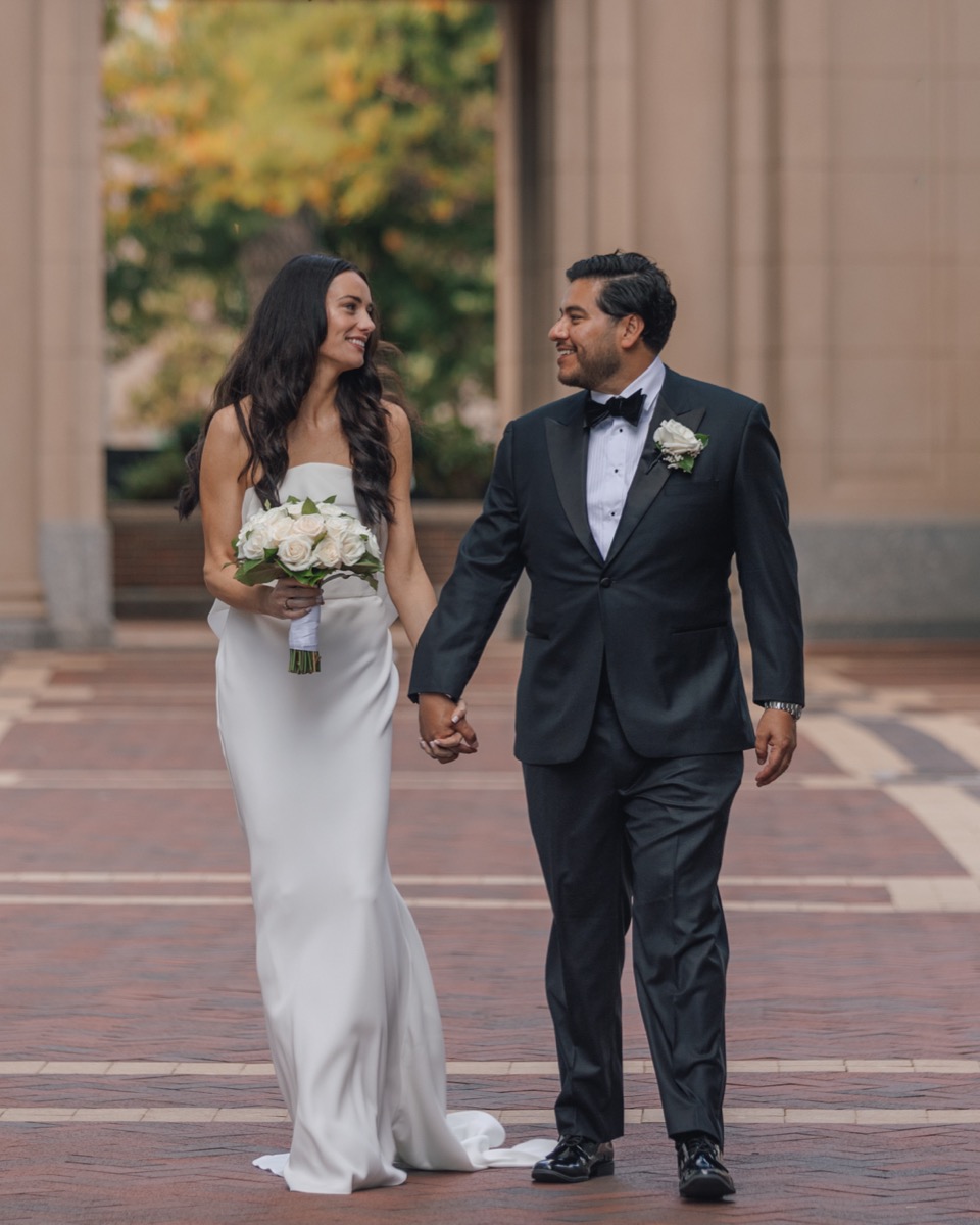 Bride and groom holding hands and laughing as they walk across the brick plaza outside the Boston Harbor Hotel