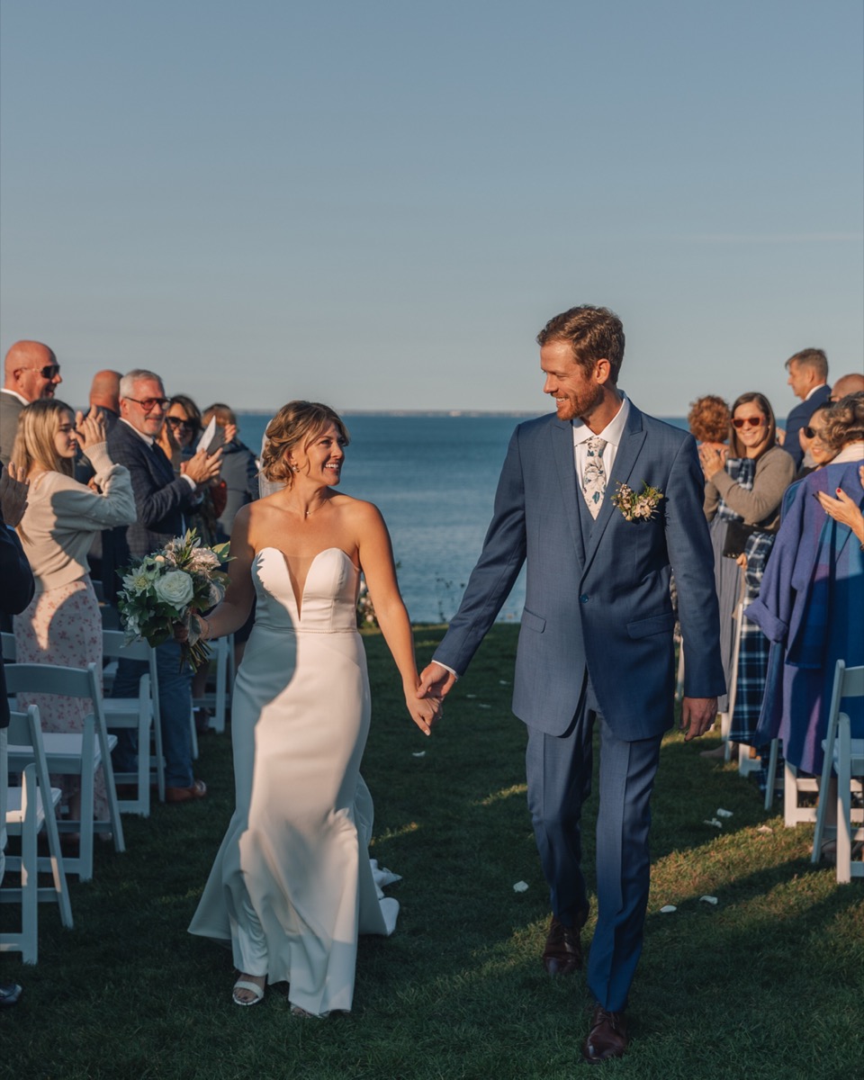 Bride and groom walking back up the aisle above the ocean as guests applaud at The Cliff House in Maine