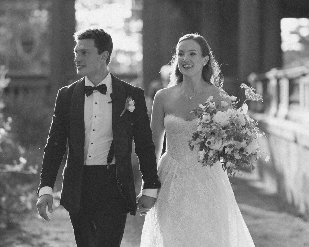 Bride and groom walking hand in hand with a bouquet, candid documentary wedding photography by Mark Davidson