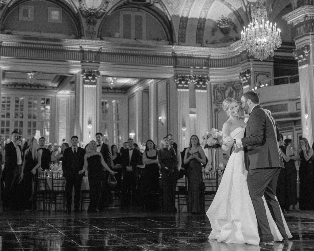 Bride and groom first dance in a ballroom as guests watch, full length single camera wedding film coverage