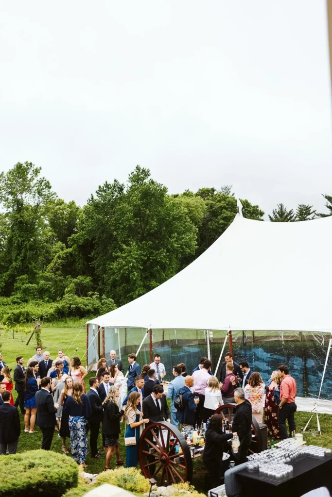 Wedding guests gather on the lawn beside a sailcloth tent at the Barn at Bradstreet Farm under a grey sky with the tree line behind