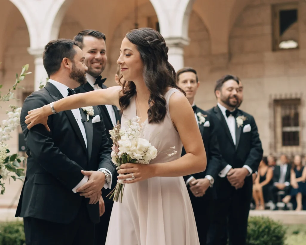 Bride and groom exchange vows in the Boston Public Library courtyard with the wedding party behind them