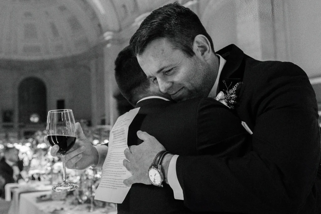 Groom embraces a guest at dinner inside the Boston Public Library, black and white