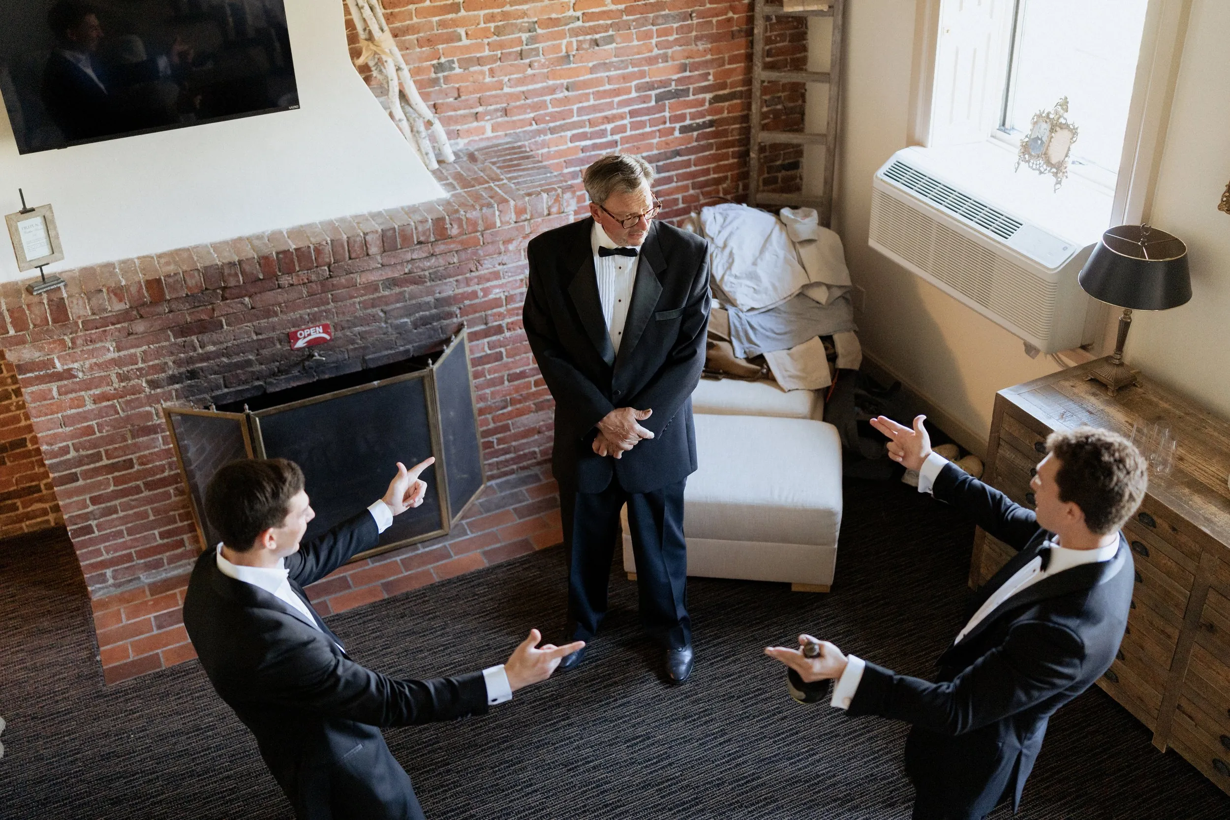 Groomsmen laughing with the father of the groom by the brick fireplace at the Garrison Inn