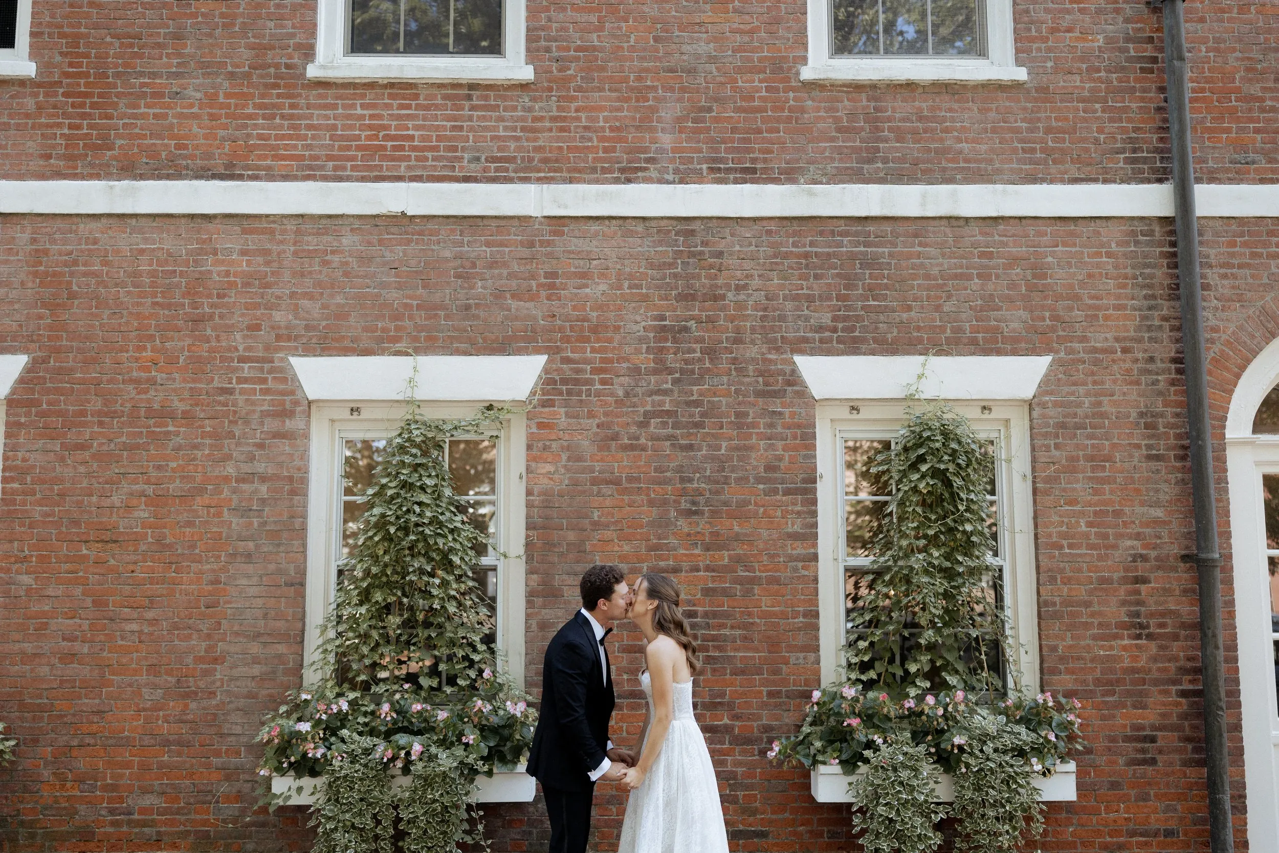 Bride and groom kissing between ivy-covered windows in Newburyport