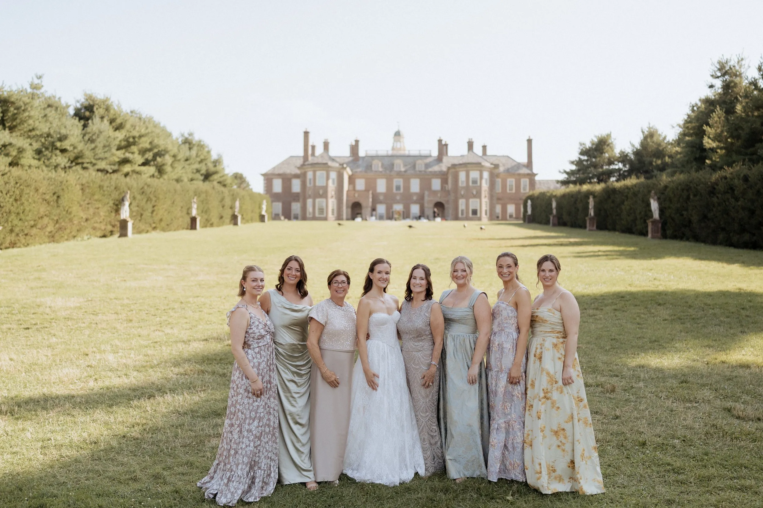 Bridesmaids in mismatched pastel gowns on the lawn in front of the Great House, Crane Estate