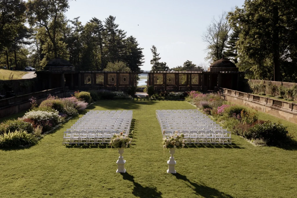 The Italian Garden at Castle Hill set for a wedding ceremony with rows of white chairs on the lawn, flower beds along the walls and the pergola at the far end