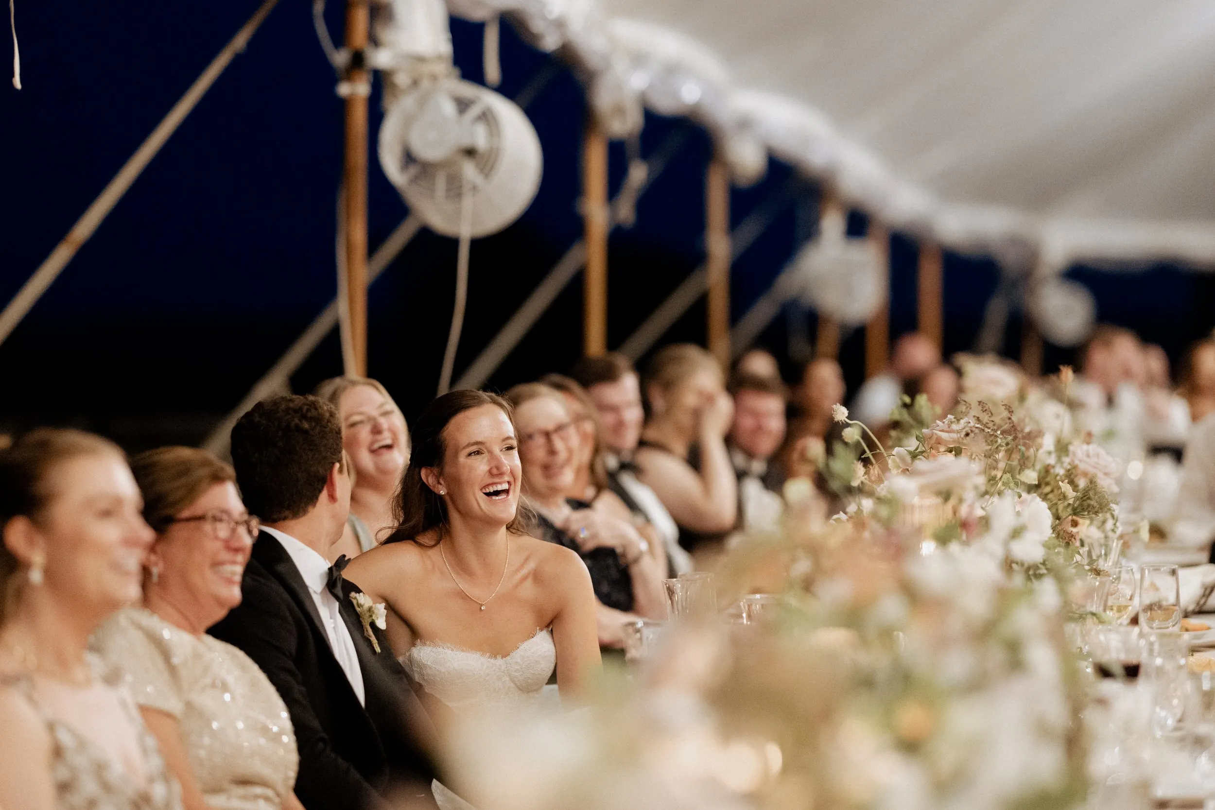 Bride laughing at the head table during the maid of honor's speech