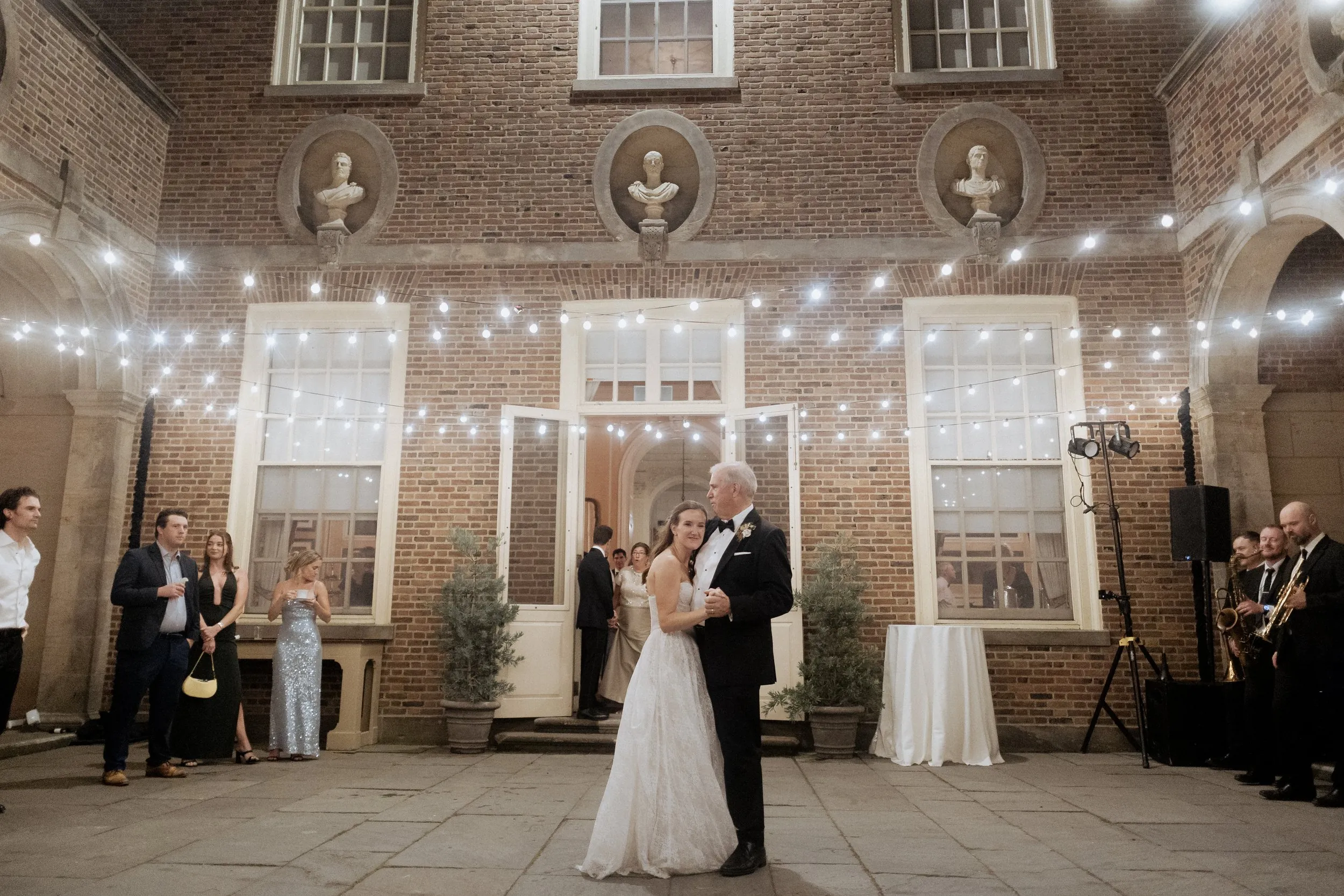 Bride dancing with her father under string lights in the courtyard at Castle Hill