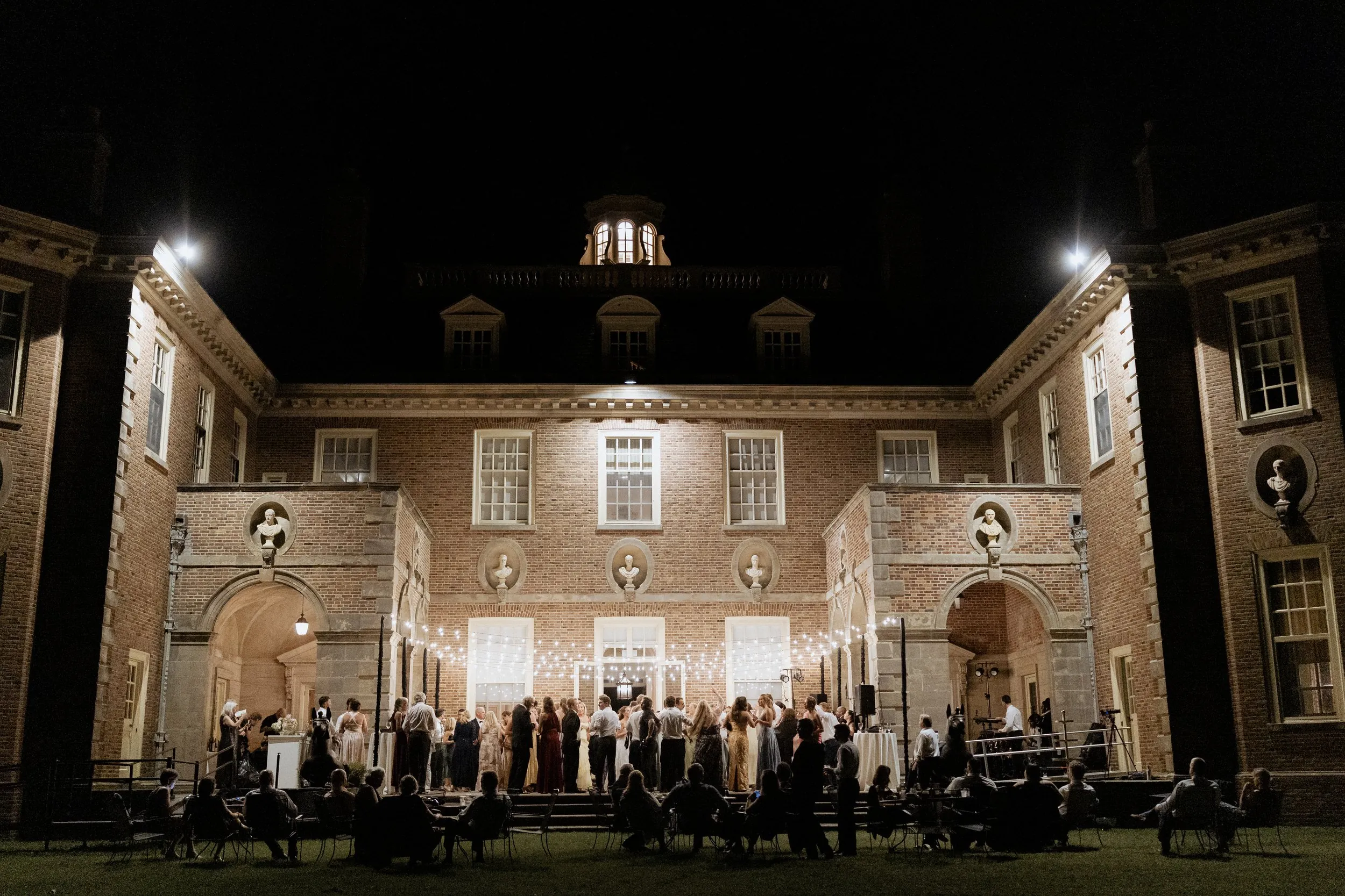 The Great House at the Crane Estate lit at night with the party in the courtyard