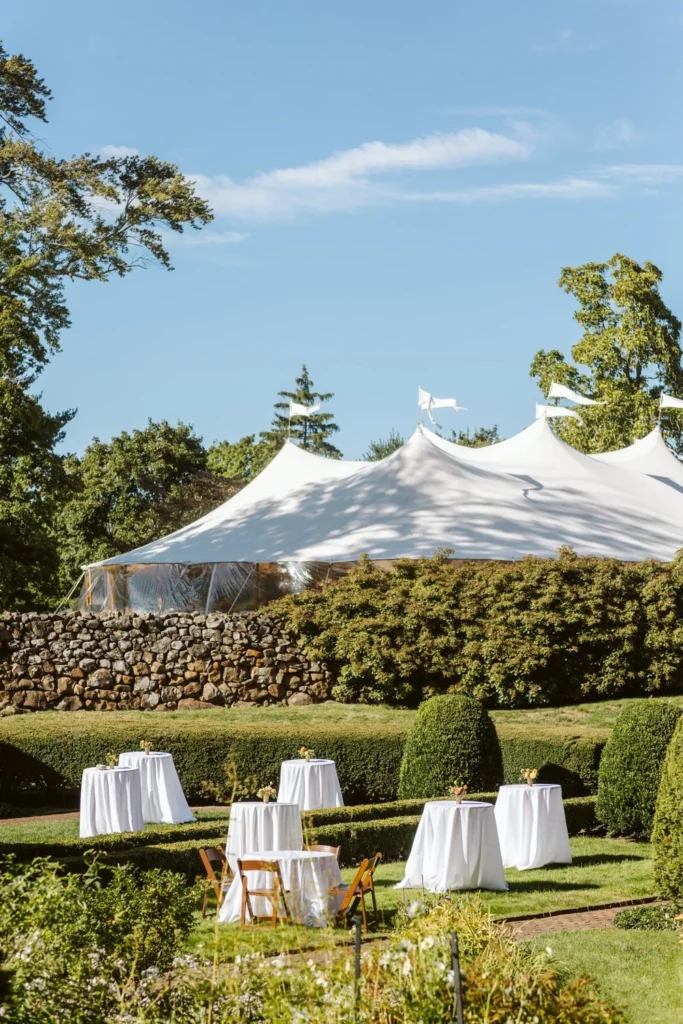 White-draped cocktail tables set among the hedges of the Sunken Garden at Hill-Stead Museum with the sailcloth tent peaks behind