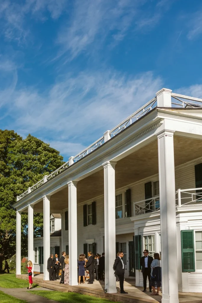 The white columned veranda of the 1901 Hill-Stead Museum house in Farmington, CT under a blue sky with wedding guests gathered below