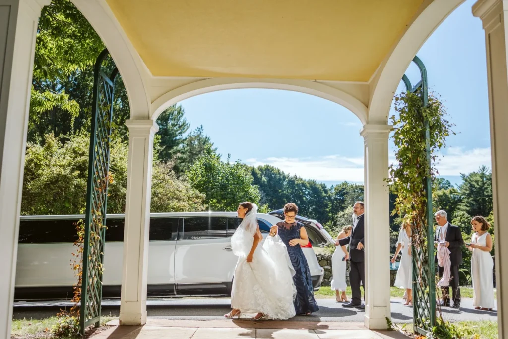 Bride steps out of a white car beneath the arched porte-cochere at Hill-Stead Museum as her family waits