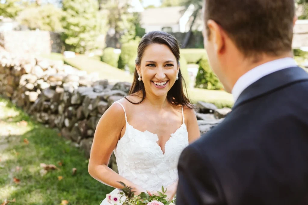Bride smiles up at the groom beside the stone garden wall at Hill-Stead Museum after their first look