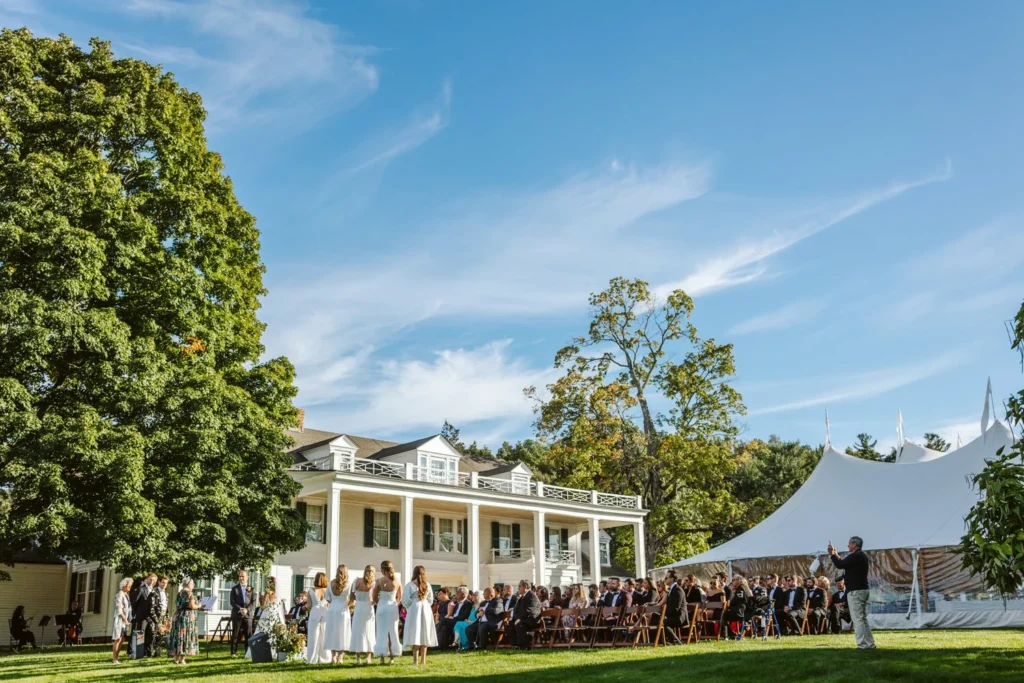 Wide view of the seated guests, the white Hill-Stead house and the sailcloth tent during a West Lawn wedding ceremony, Farmington, CT
