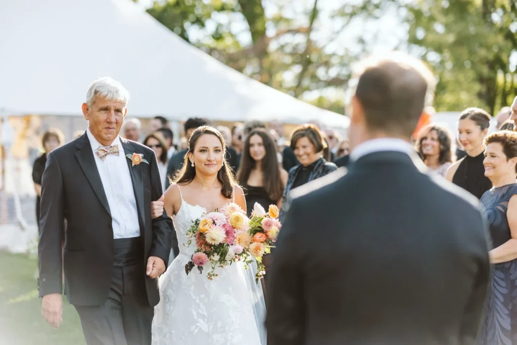 Bride on her father's arm reaches the groom at the altar under the trees at Hill-Stead Museum with guests and the tent behind