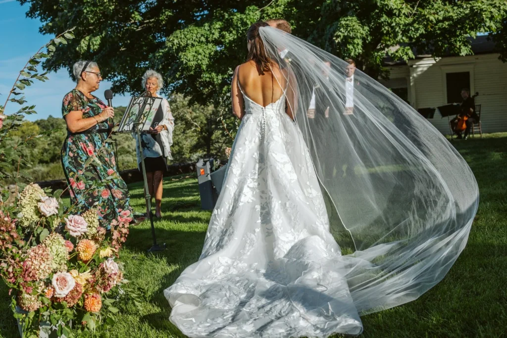 The bride's long veil lifts in the wind as she walks back up the aisle past the florals and musicians at Hill-Stead Museum