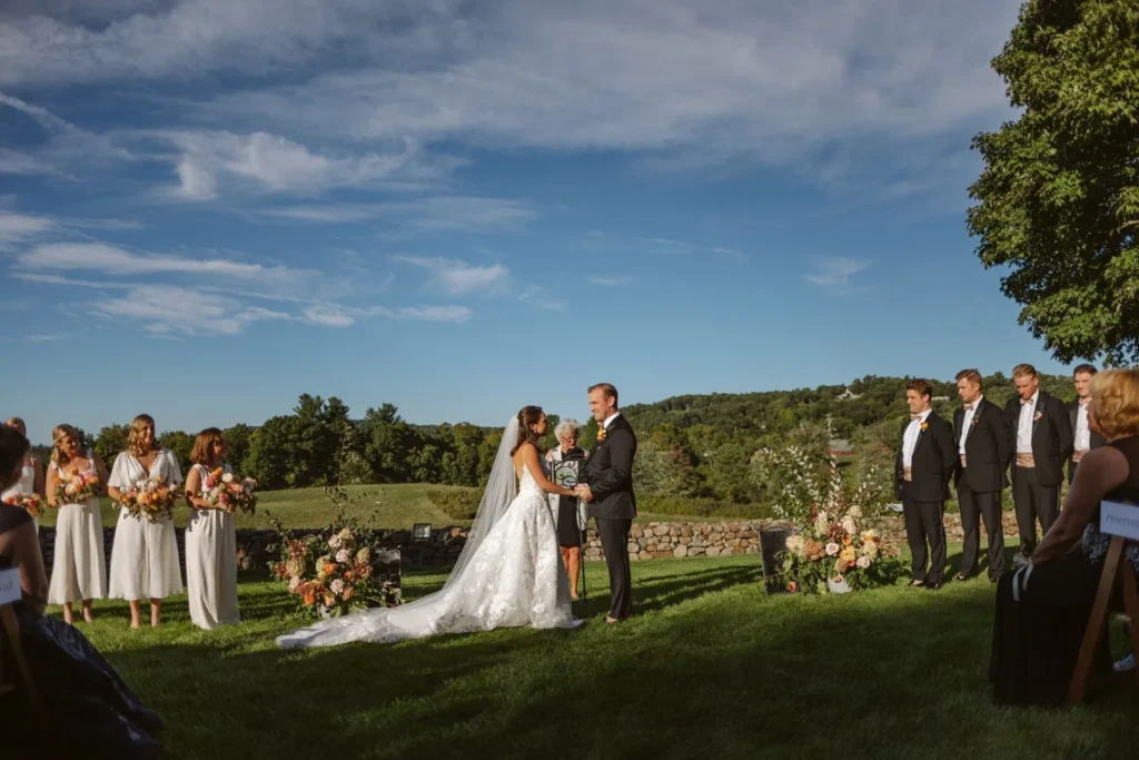Bride and groom exchange vows on the West Lawn at Hill-Stead Museum with the wedding party either side and the meadow and Litchfield Hills behind them