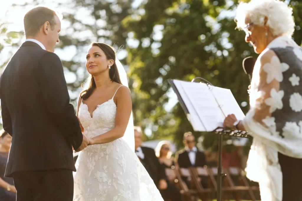 Bride and groom hold hands and exchange vows with the officiant reading from a music stand on the West Lawn at Hill-Stead Museum