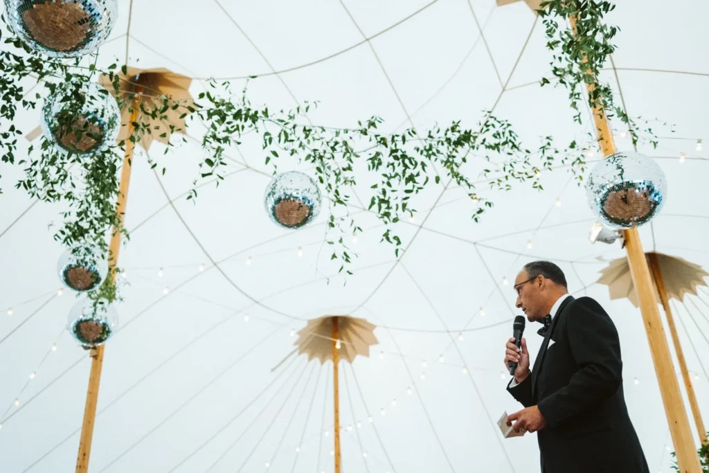 A guest gives a toast beneath hanging greenery and disco balls inside the sailcloth tent at Hill-Stead Museum