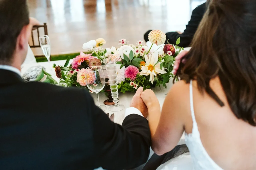 Bride and groom hold hands at the head table with dahlia arrangements at a Hill-Stead Museum wedding