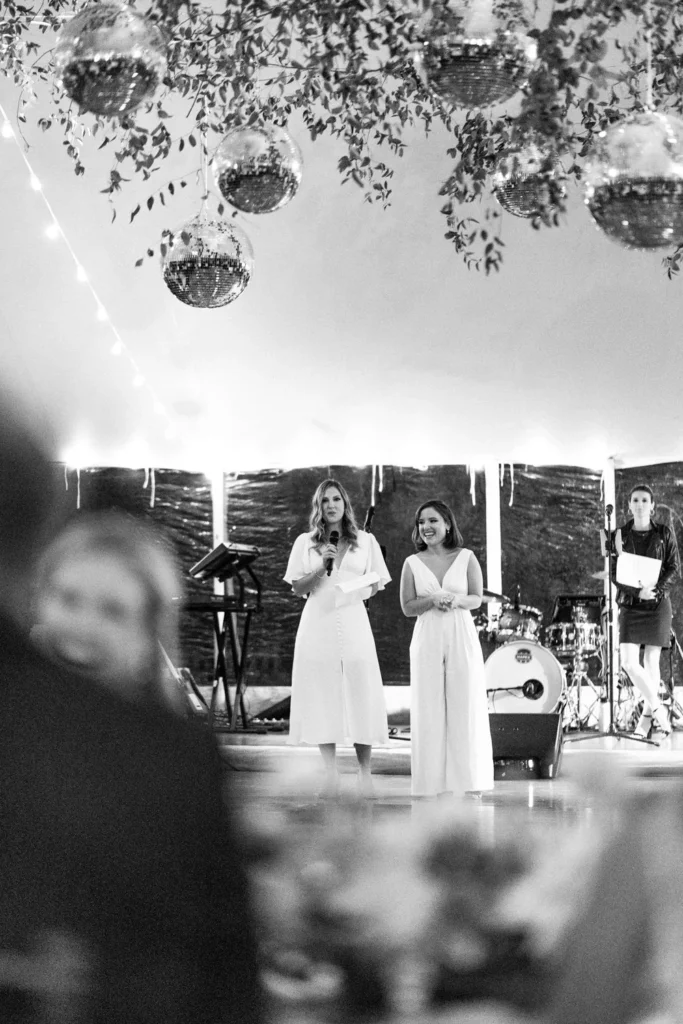 Black and white photo of a speech given beneath the disco balls and greenery inside the tent at Hill-Stead Museum