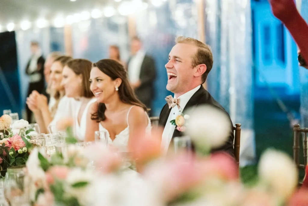 Bride and groom laugh at the head table during toasts under the tent at Hill-Stead Museum with dahlias in front of them
