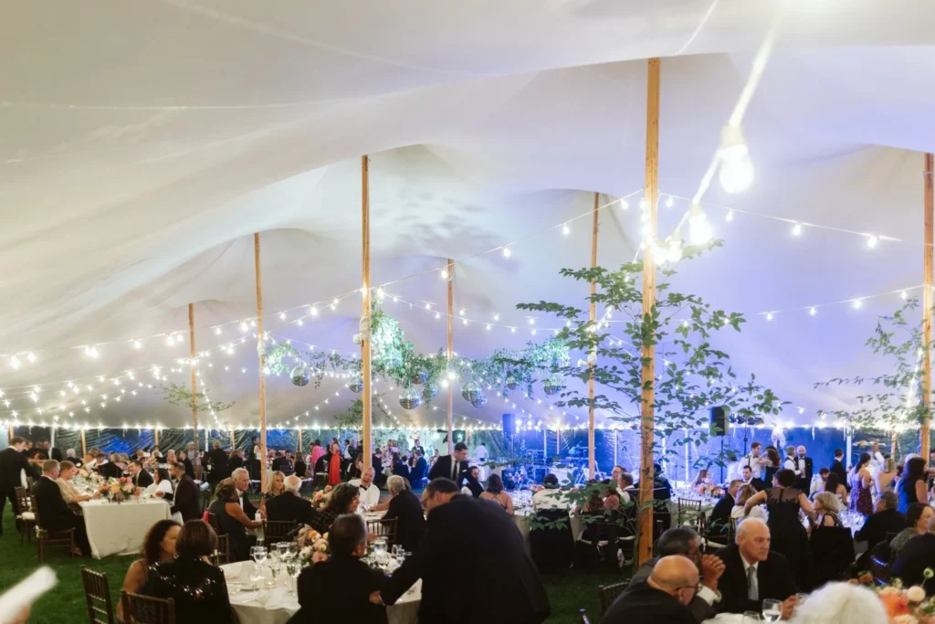 Inside a sailcloth Sperry tent at Hill-Stead Museum during a wedding reception with string lights, greenery on the poles and guests seated at dinner