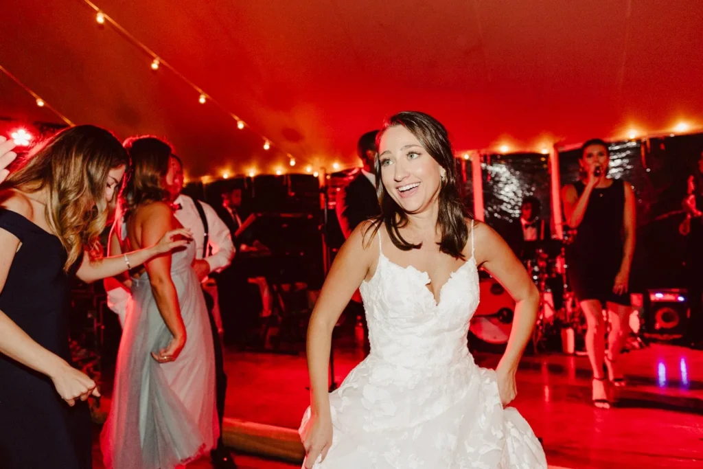 Bride dances with friends under red light and string lights inside the tent at Hill-Stead Museum