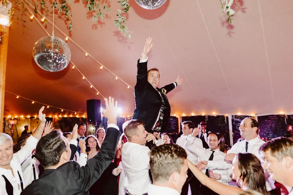Groom rides on a friend's shoulders with arms raised above the dance floor at Hill-Stead Museum