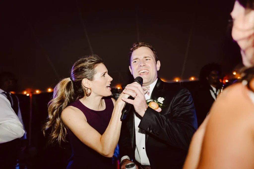 Groom sings into the microphone beside the band's singer under the tent at Hill-Stead Museum