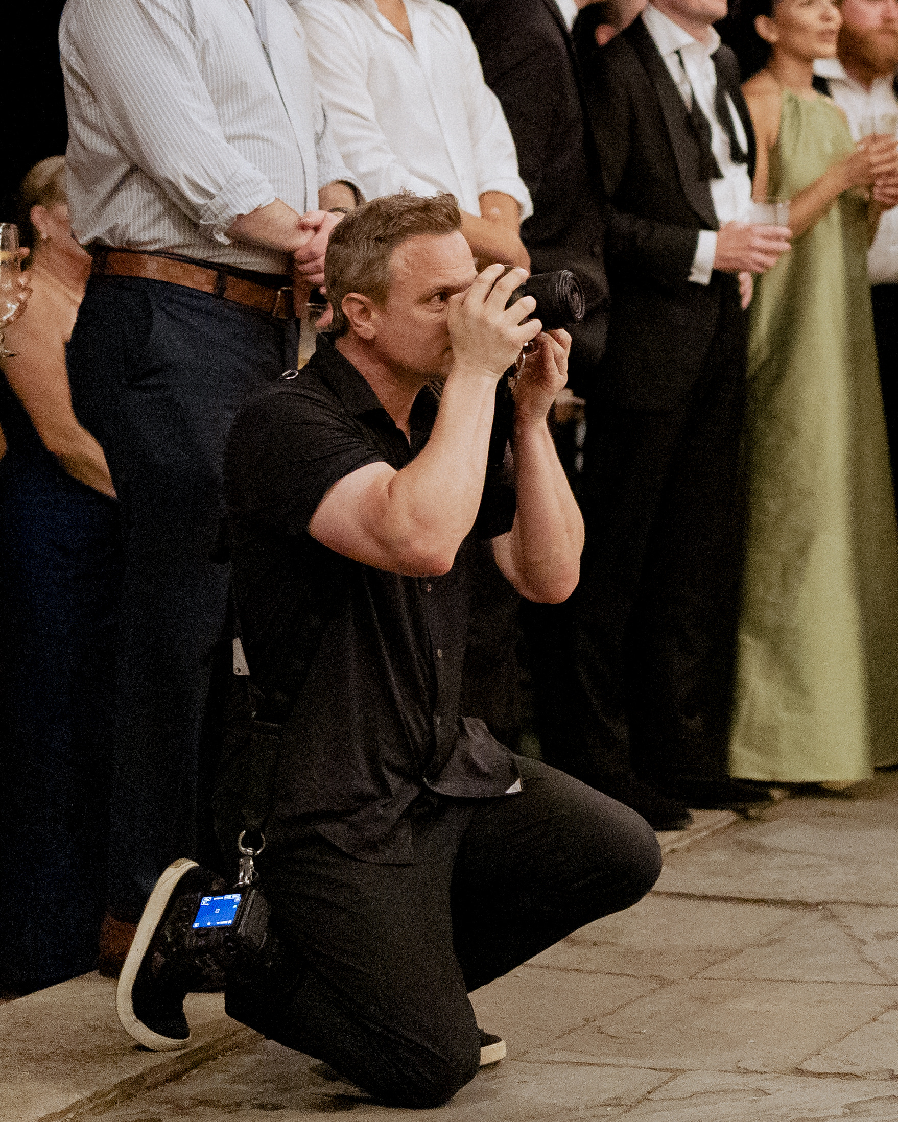 Mark Davidson kneeling among guests, photographing a Boston wedding reception
