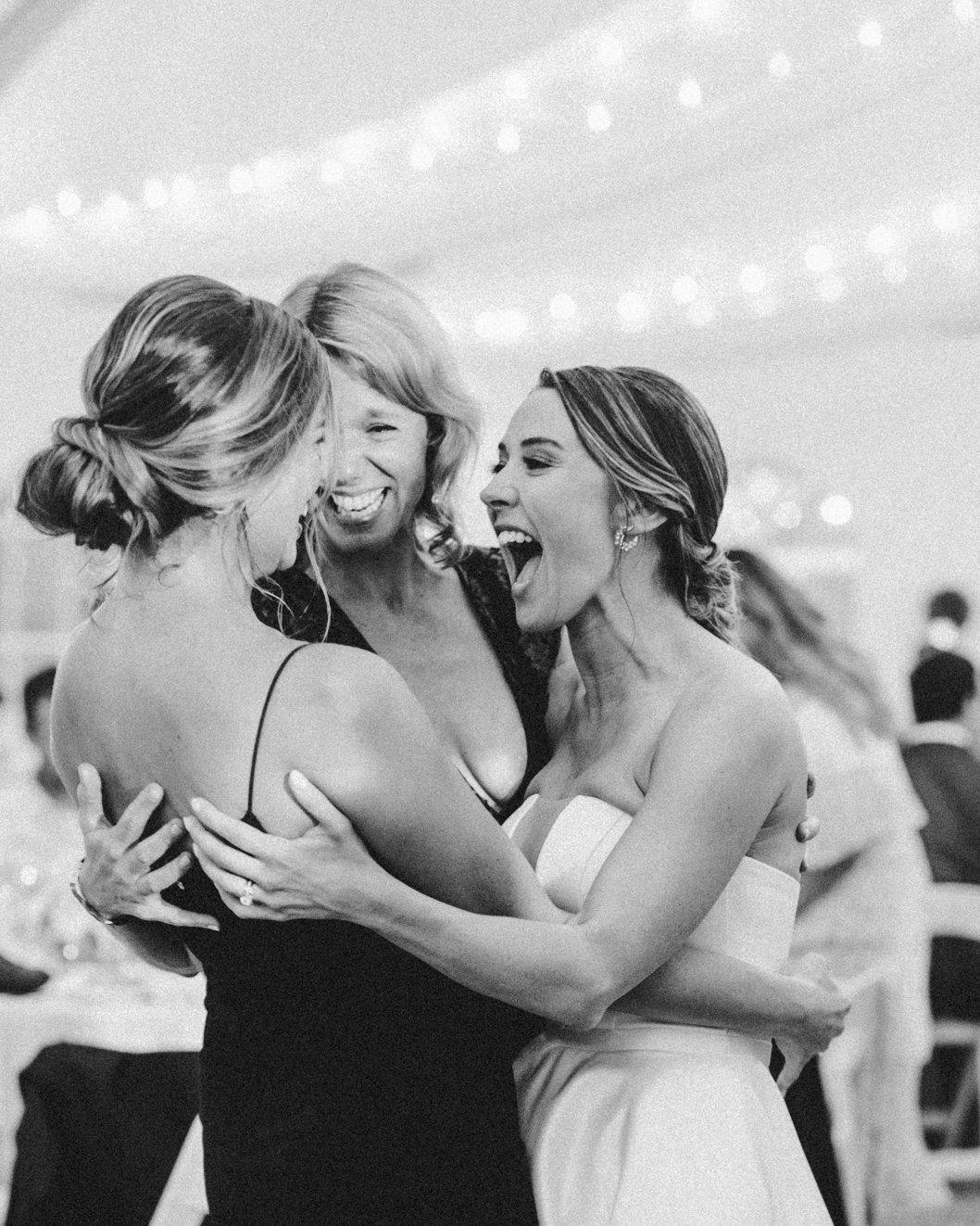 A bride laughs with two friends under string lights at Misselwood in Beverly
