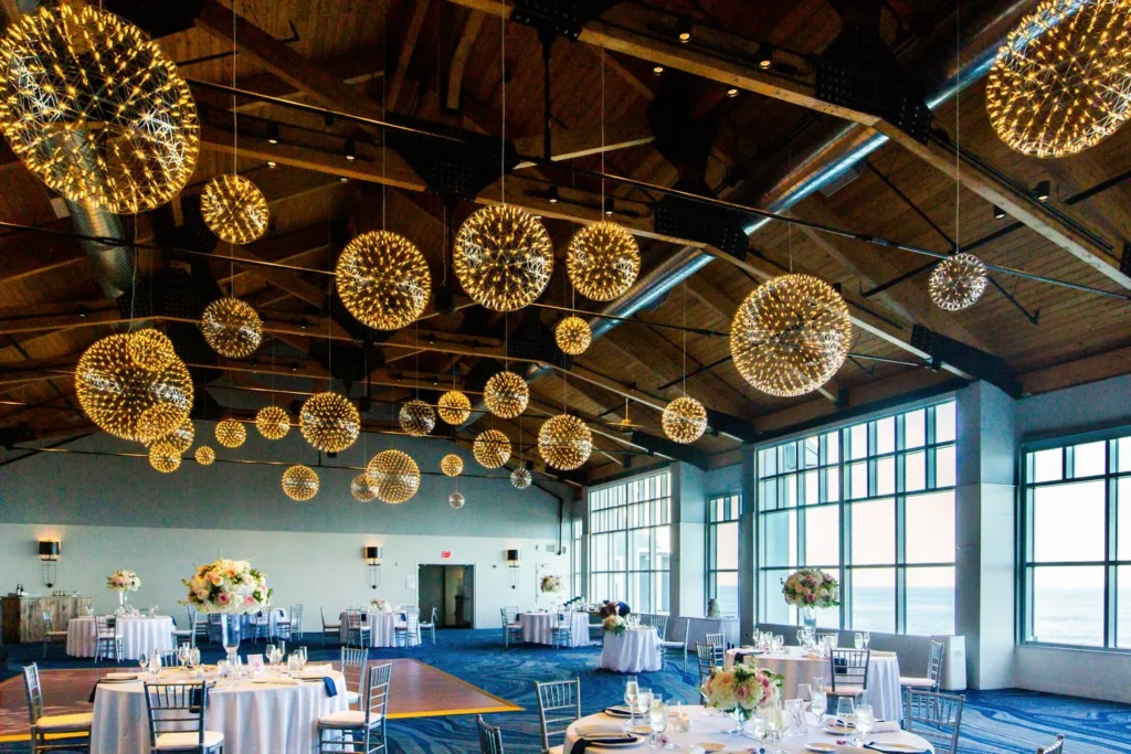 The Atlantic Ballroom at Cliff House Maine set for a wedding reception with round tables, blue linens and spherical chandeliers under the cedar ceiling