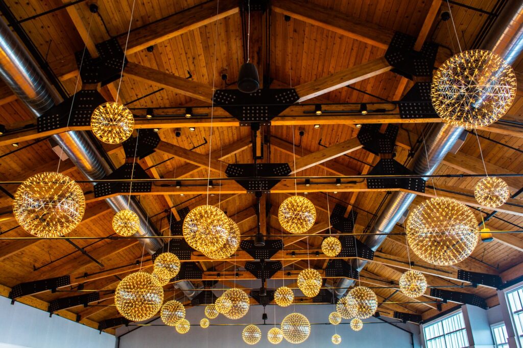 The beamed cedar ceiling of the Atlantic Ballroom at Cliff House Maine with a cluster of glowing spherical chandeliers