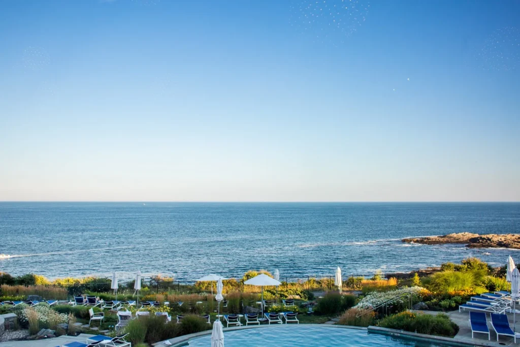 The heated infinity pool at Cliff House Maine seen from a guest-room balcony with the Atlantic Ocean and the rocky shore beyond