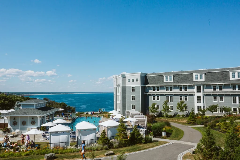 The grey shingled main building, pool deck and lawns of Cliff House Maine on a clear day with the ocean in the distance