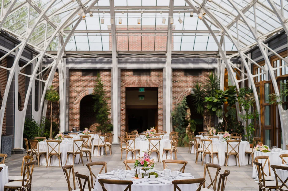 The Orangerie at Tower Hill Botanic Garden set for a wedding dinner with round tables, crossback chairs and the glass roof overhead