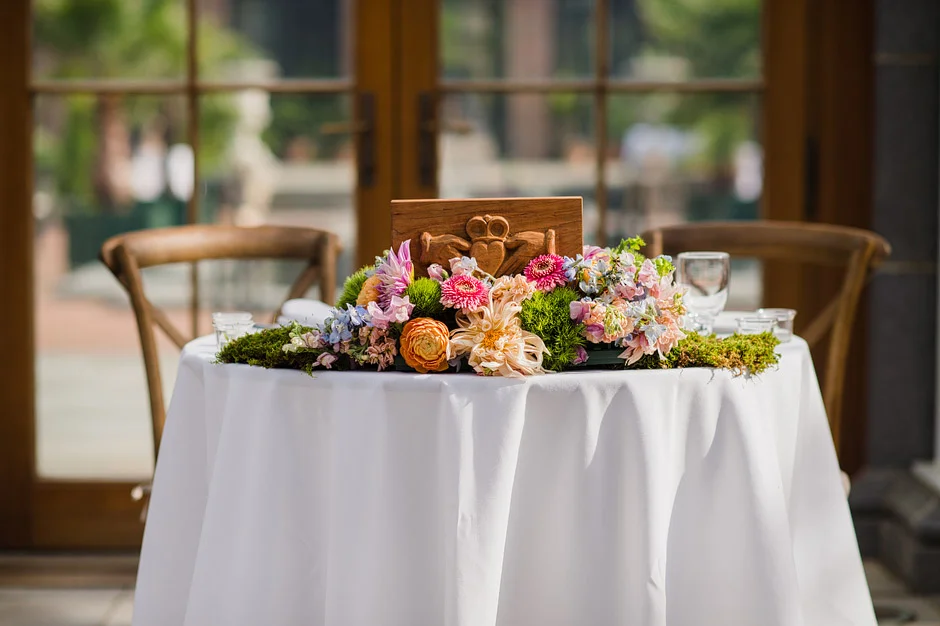 Sweetheart table with a low arrangement of coral, pink and blue garden flowers on moss in front of the Orangerie doors at Tower Hill Botanic Garden