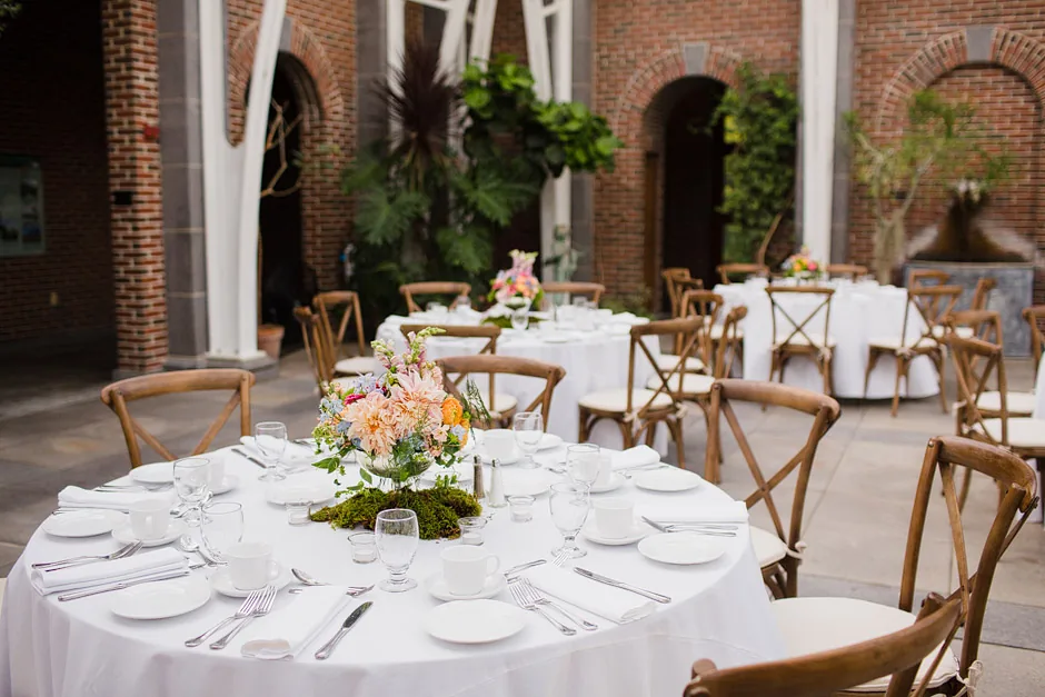 Round tables with white linens, crossback chairs and garden florals set on the brick courtyard outside the Orangerie at Tower Hill Botanic Garden