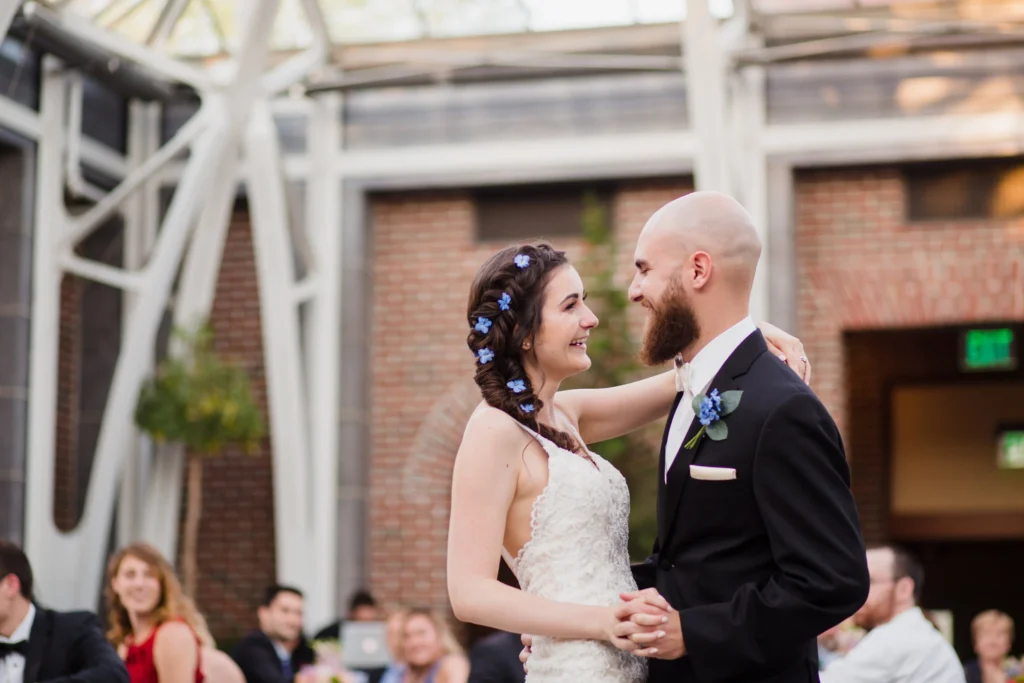 Bride and groom share their first dance inside the Orangerie at Tower Hill Botanic Garden with the white steel arches and brick walls behind them