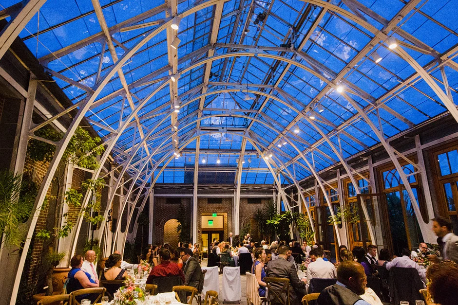 The steel arches and glass roof of the Orangerie at Tower Hill Botanic Garden turning deep blue at dusk over a wedding reception