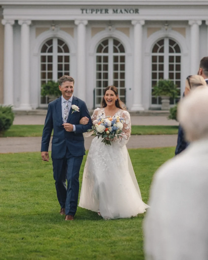 Bride walks down the aisle with her father across the front lawn at Tupper Manor